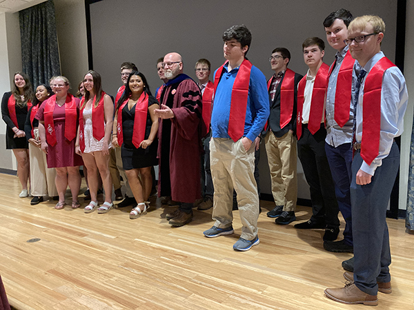 Group of students standing on stage with red sashes