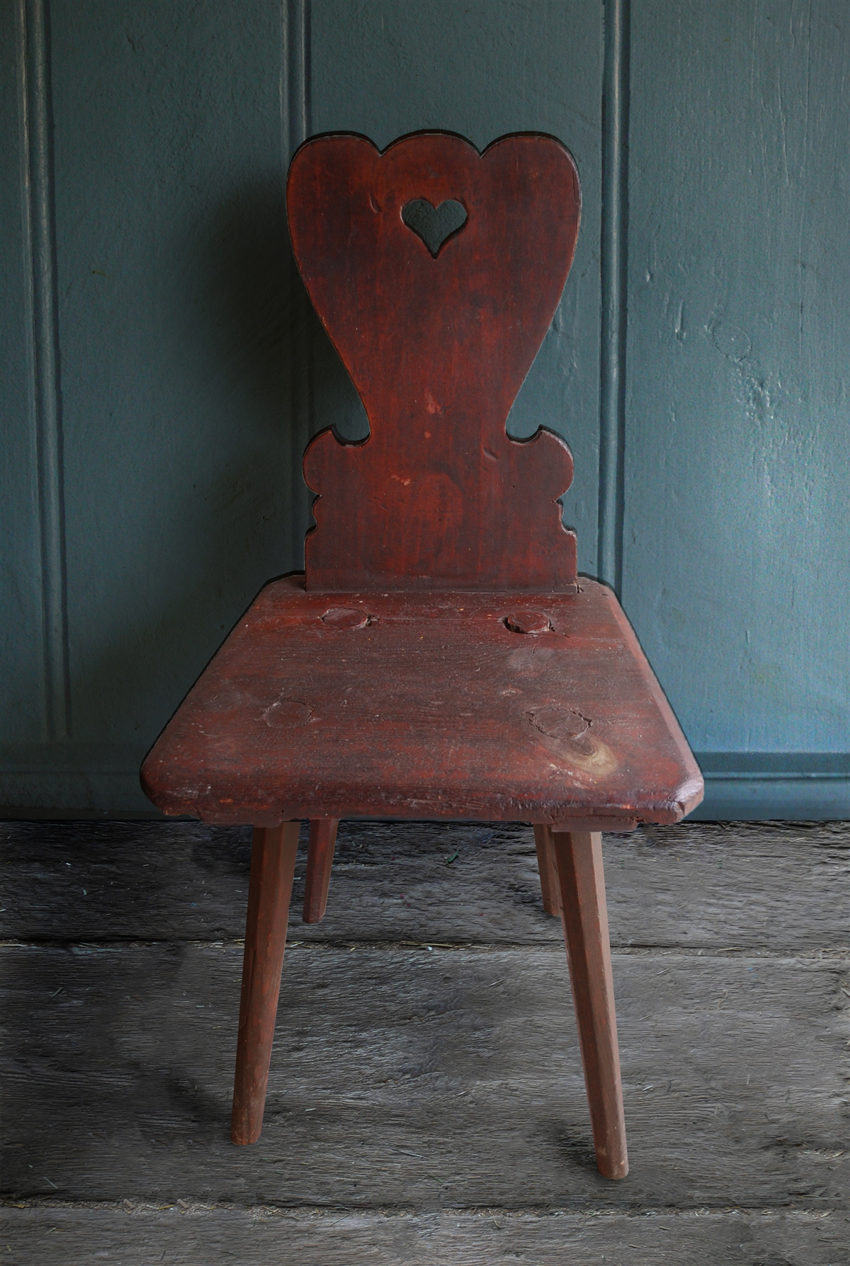 A small wooden chair with four legs, a square seat, and a curved, carved back with a heart cutout at the top.