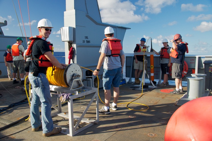 Group of male students on the deck of a research vessel wearing safety gear