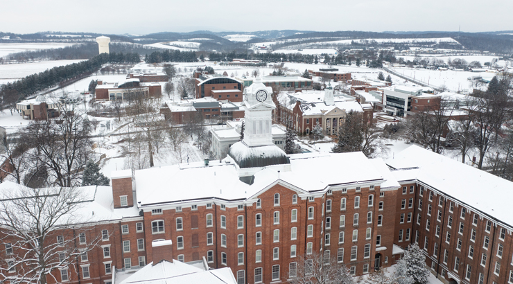 Old main in foreground wiht north campus buildings and countryside beyond covered in snow.