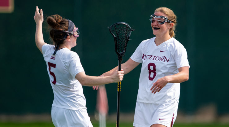 Two women's lacrosse players celebrating on the field.