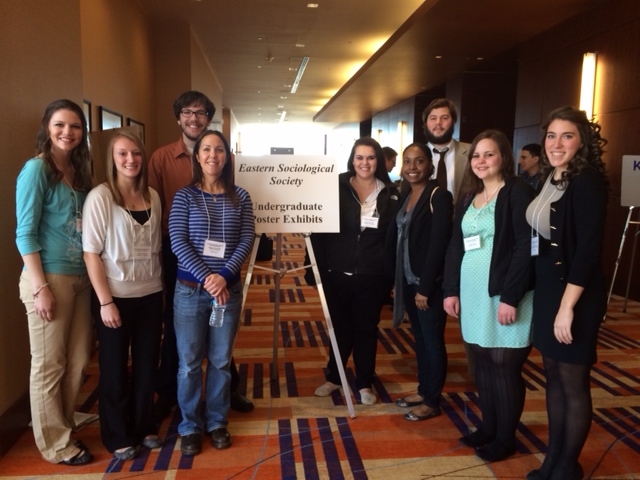 Students and professor at the Eastern Sociological Society Conference in Baltimore, smiling as a group in the entrance to undergraduate poster exhibits