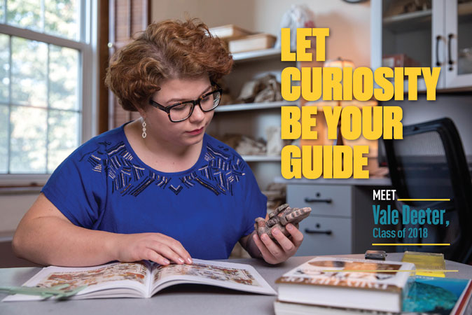 A female student studying an artifact with a reference guide open on the table in front of her. Text reads "Let curiosity be your guide. Meet Vale Deeter, Class of 2018." 