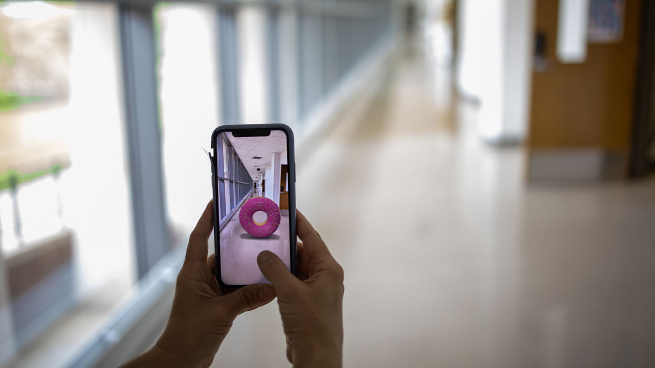hand holding a smartphone in front of a hallway, photoshopping a doughnut into a picture of the hall