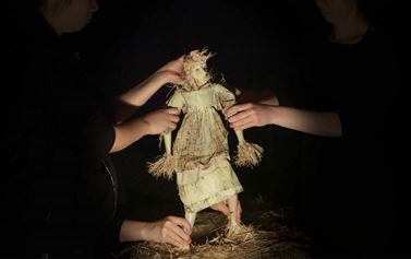 Three pairs of hands gripping a scarecrow doll in the dark 