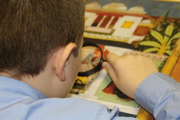 Student examining artwork with magnifying glass.