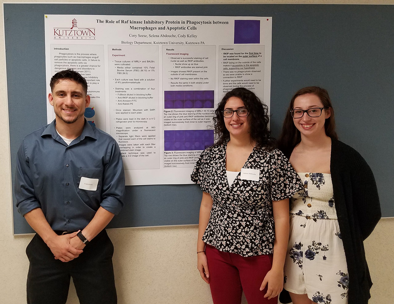 Three students standing in front of a poster on "the role of Raf kinase inhibitory protein in phagocytosis between macrophages and apoptotic cells."