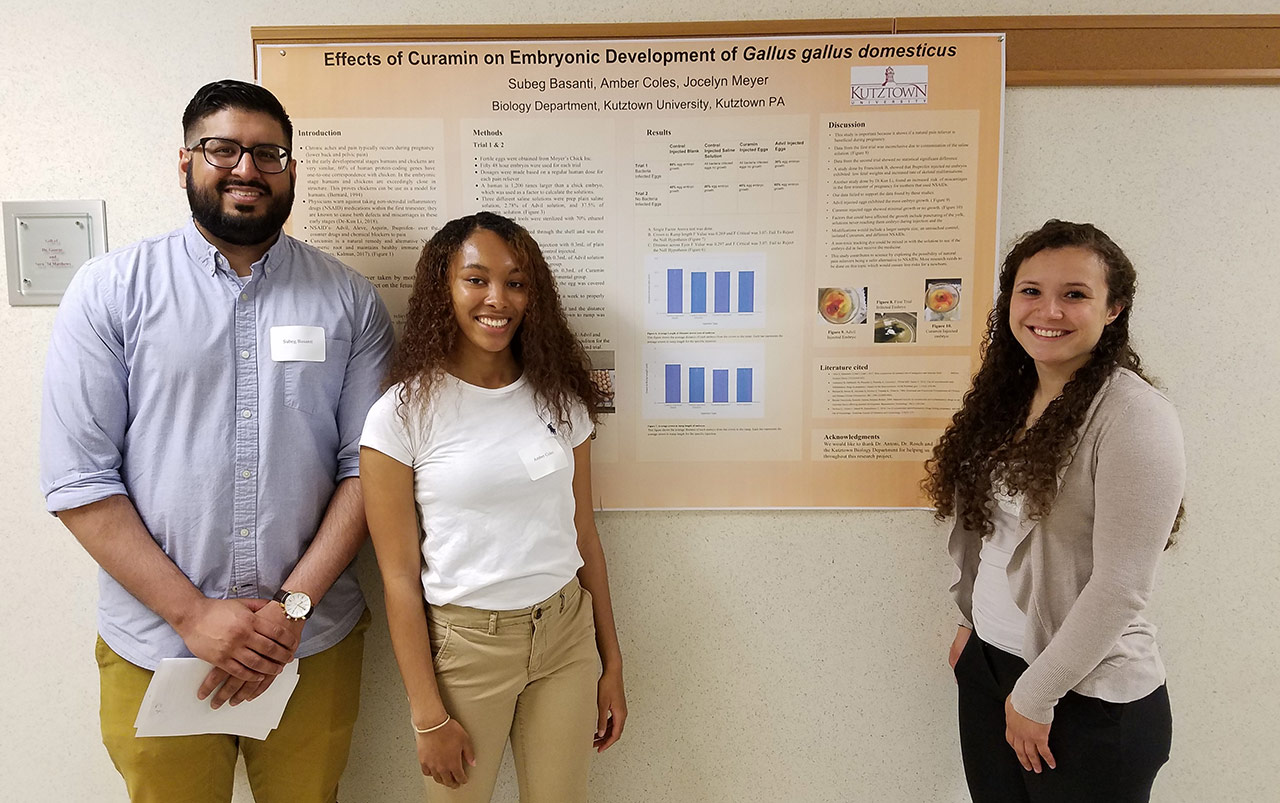 Three students stand beside a poster on the "Effects of Curamin and Embryonic development of gallus gallus domesticus."