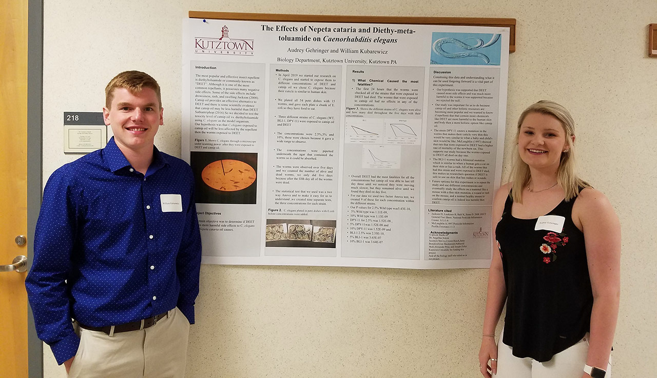 A female and male student stand on either side of a poster on the "Effects of Nepeta cataria and Diethy-meta-toluamide on Caenorhabditis elegans." 