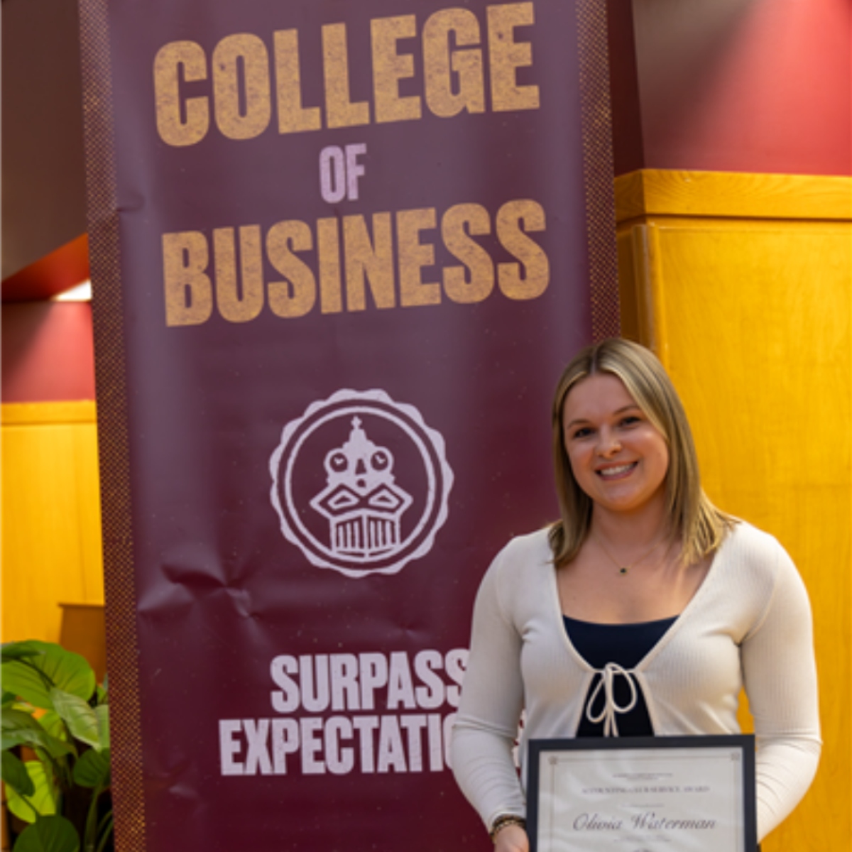 Student Olivia Waterman in front of maroon and gold College of Business banner with award