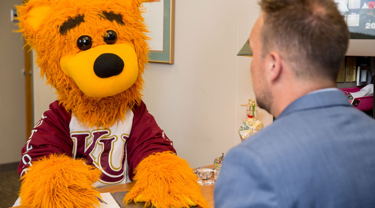 Image of Avalanche the mascot writing on a pad of paper sitting across the desk from a male career center employee wearing a blue suit jacket