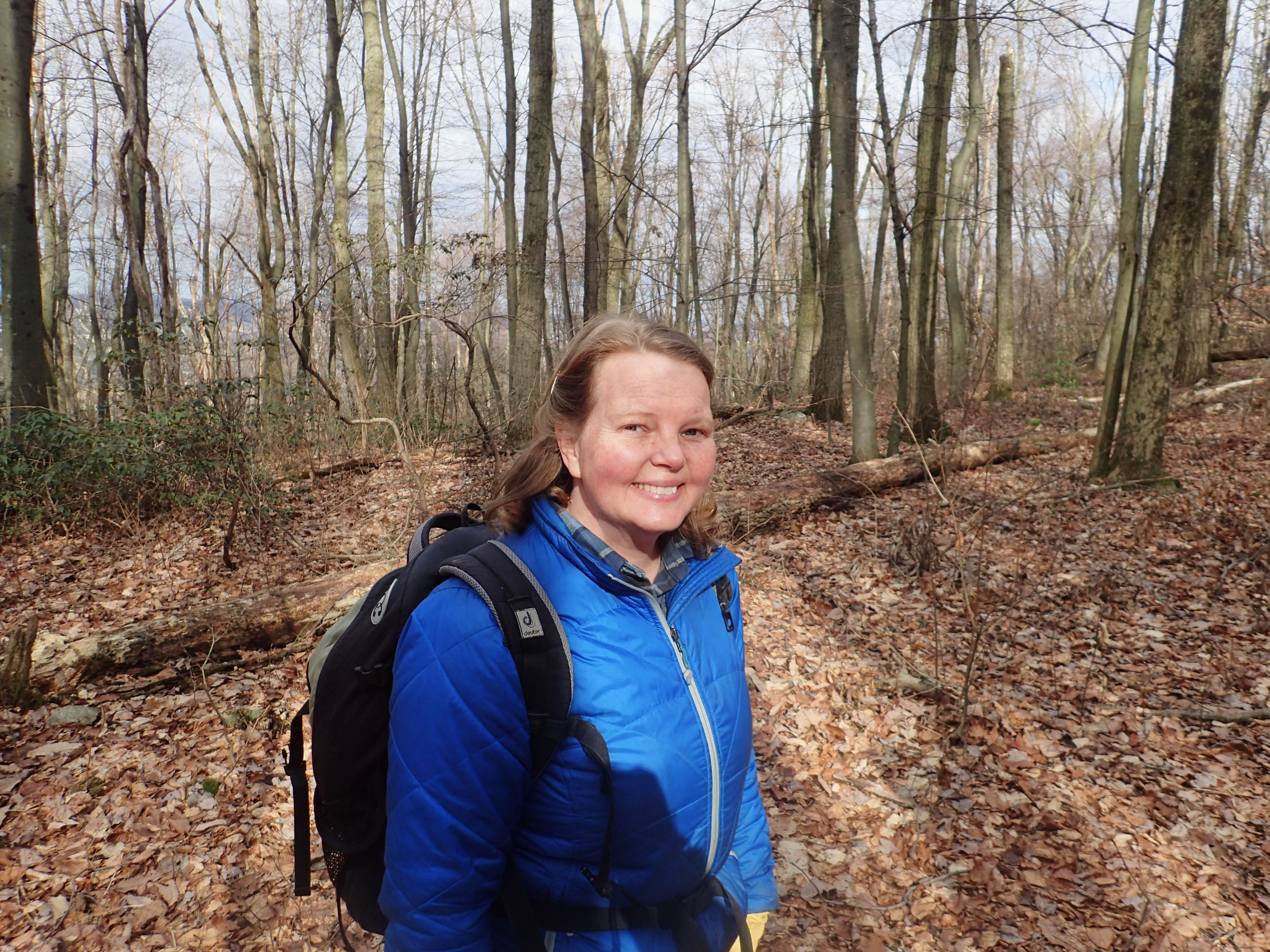 Dr. Erin Kraal, hiking in a forest in autumn, surrounded by bare trees and fallen leaves