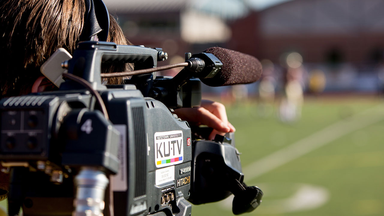 Closeup on KU-TV camera operator filming a football game on campus