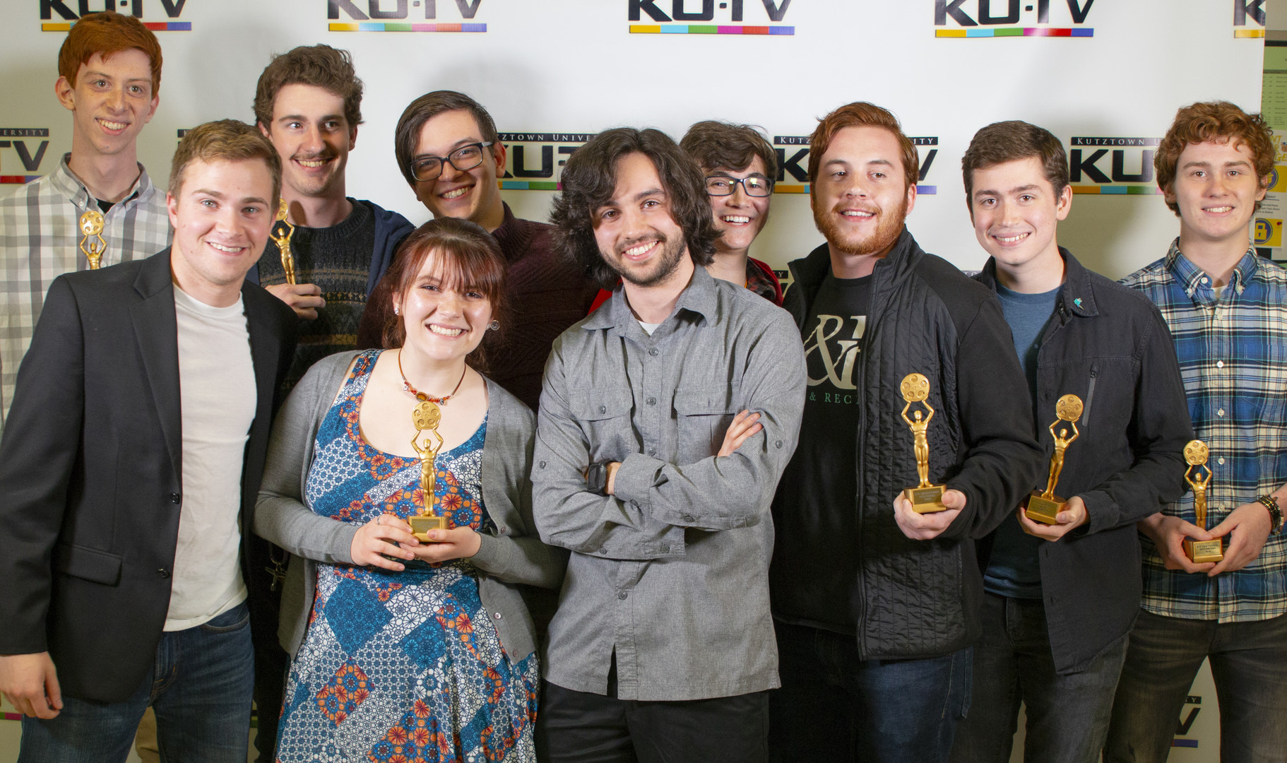 Kutztown University Film Festival group holding up their awards and smiling together in front of KUTV wallpaper 