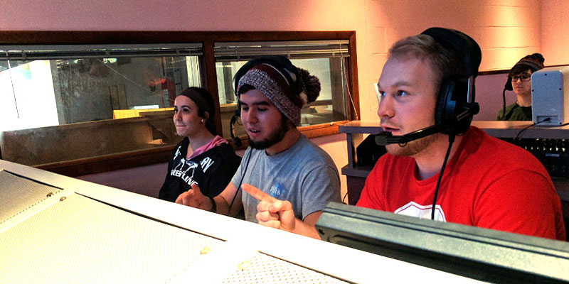 Four students working in a control room and wearing headsets 