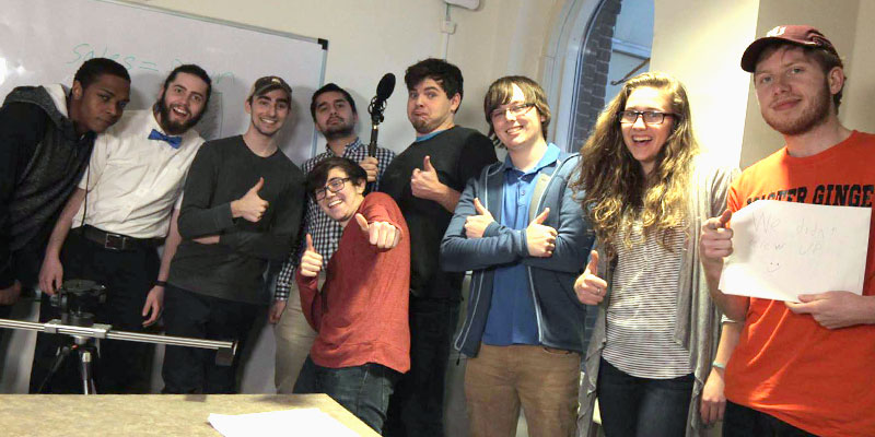 Film students smiling and holding their thumbs up in the corner of a classroom 