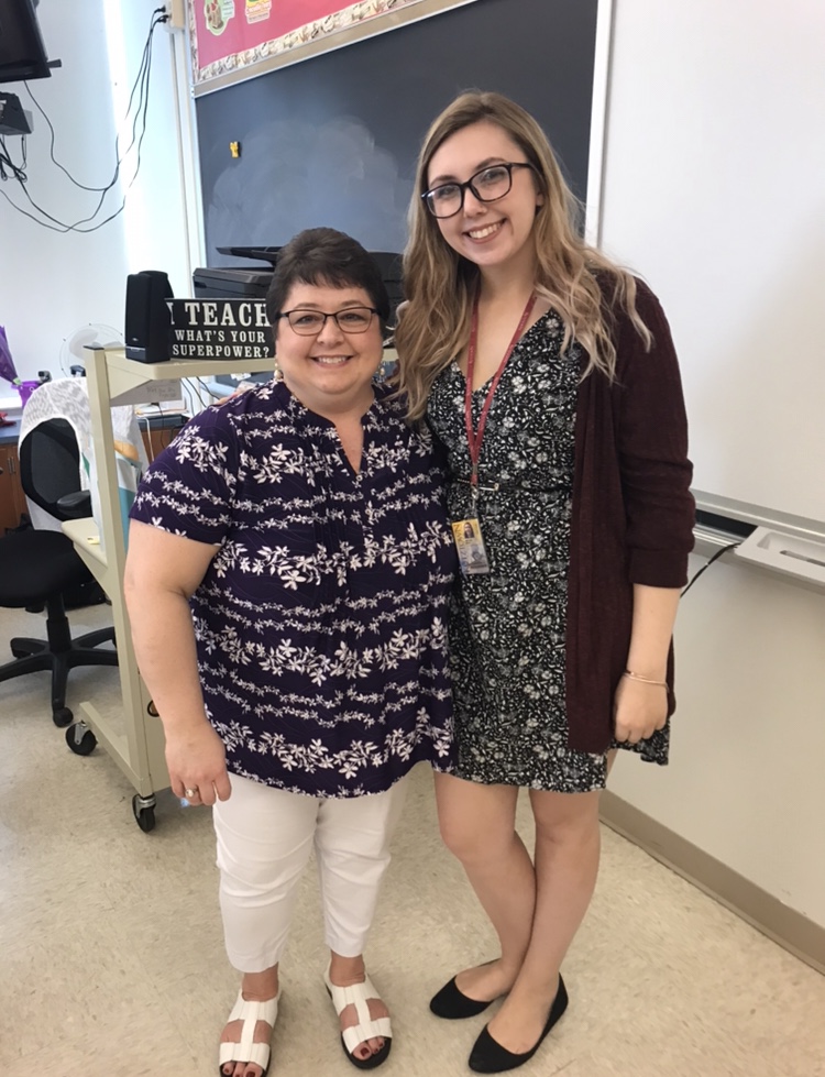 Professor and student teacher smiling together in a classroom with their arms around each other