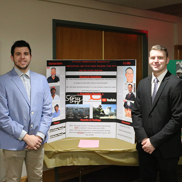 Two students standing on either side in front of a poster presentation
