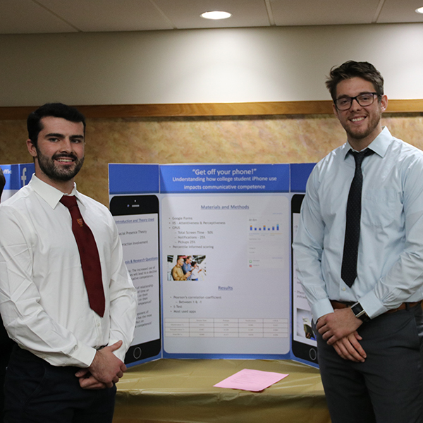 Two students standing on either side in front of a poster presentation titled "Get off your phone!" 