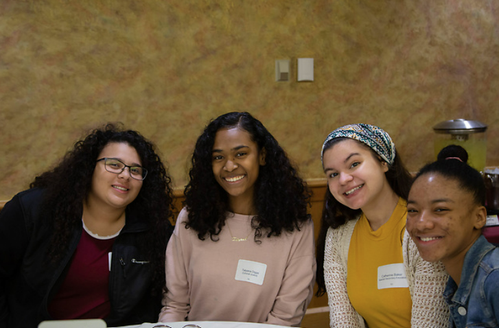 4 students sitting at a round table smiling 