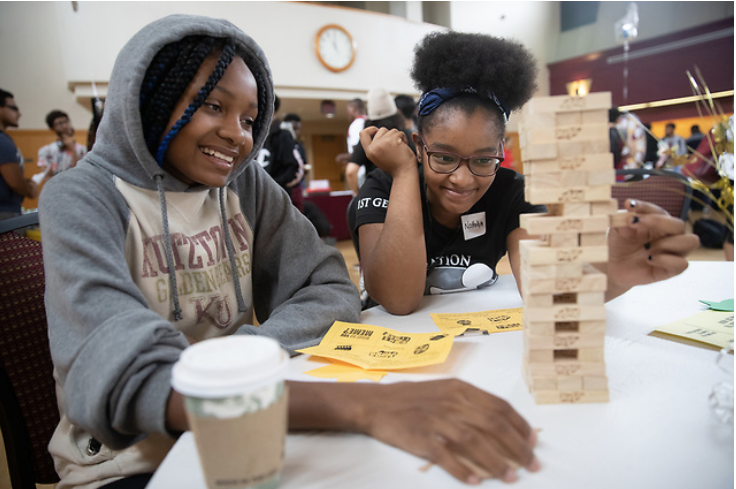two African American female students sitting at round table playing Jenga