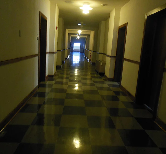 A long, empty hallway in Old Main, lit by yellow lights with a window in the background casting blueish light