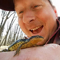 Dr. Chris Habeck holding a frog on his arm smiling