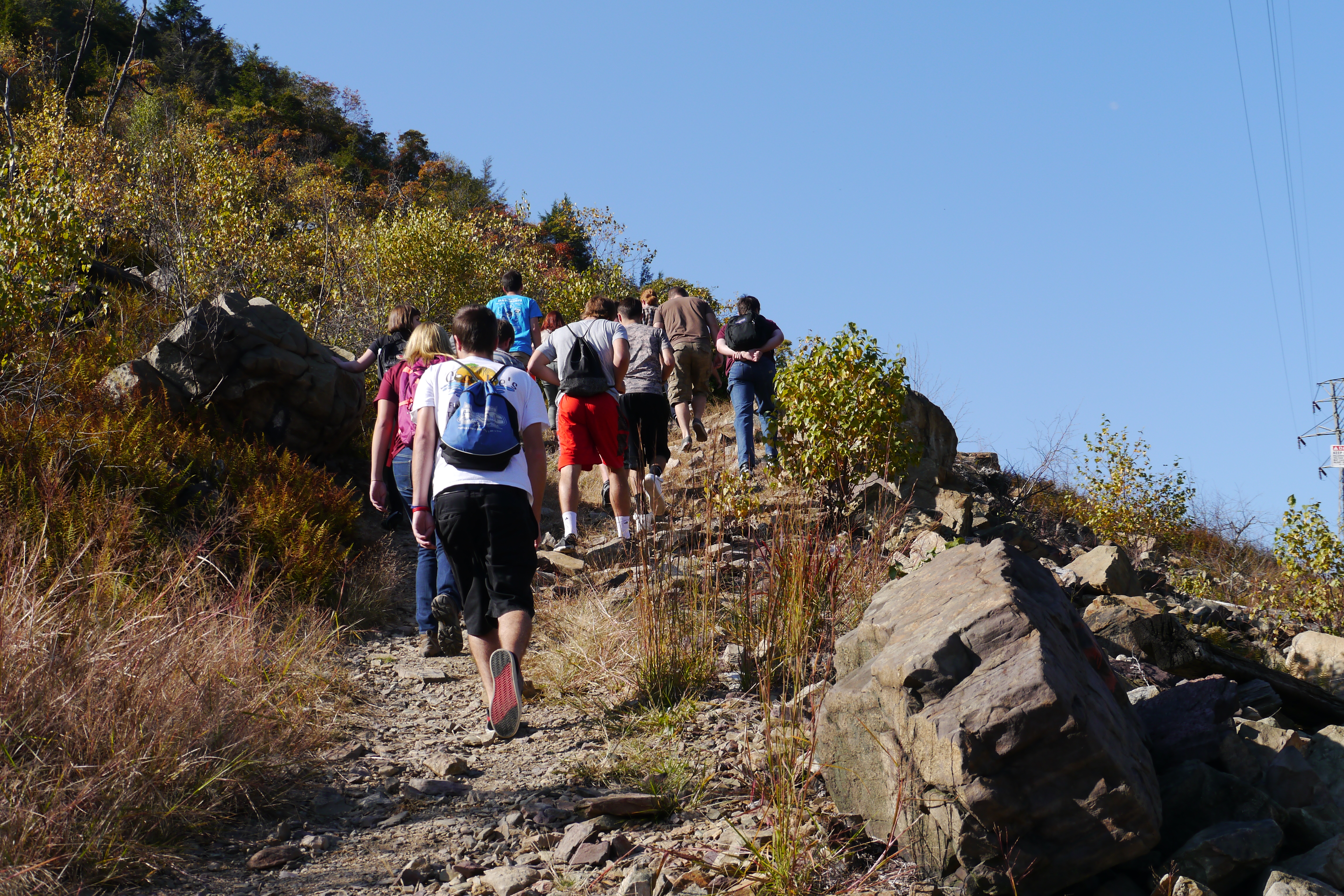 students hiking up a small footpath on the side of a grassy, rocky mountain
