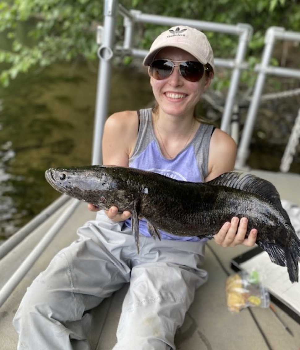 Emily Bohn wearing black v-neck shirt standing in front of large green research equipment