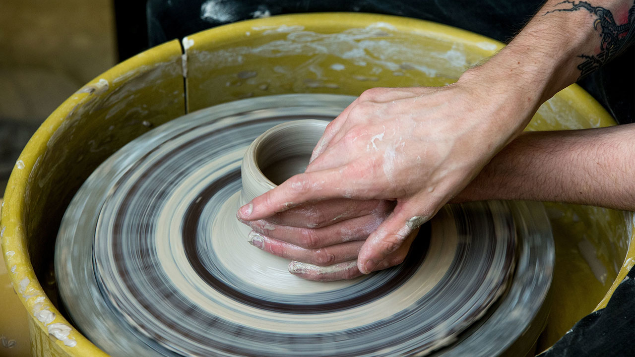 Closeup on a pair of hands working on a clay bowl on a wheel 