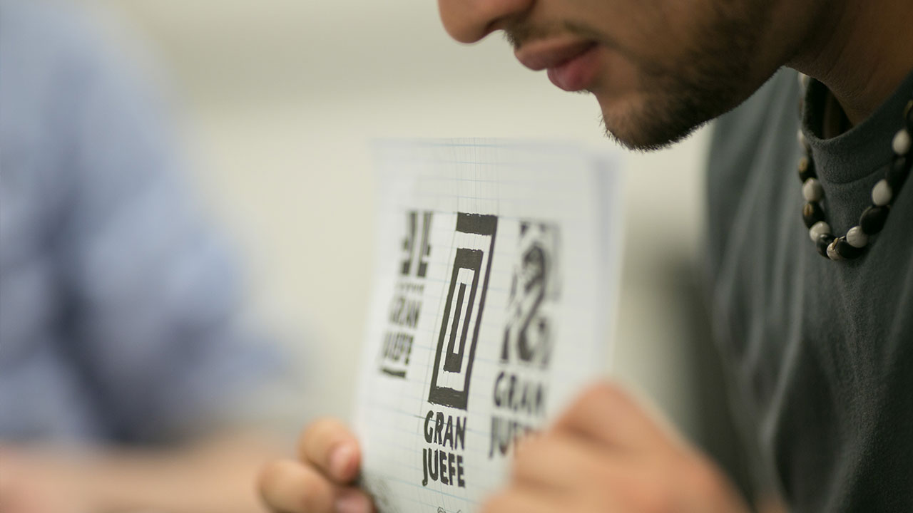 Student holding a piece of paper with symbols and the words "gran juefe"