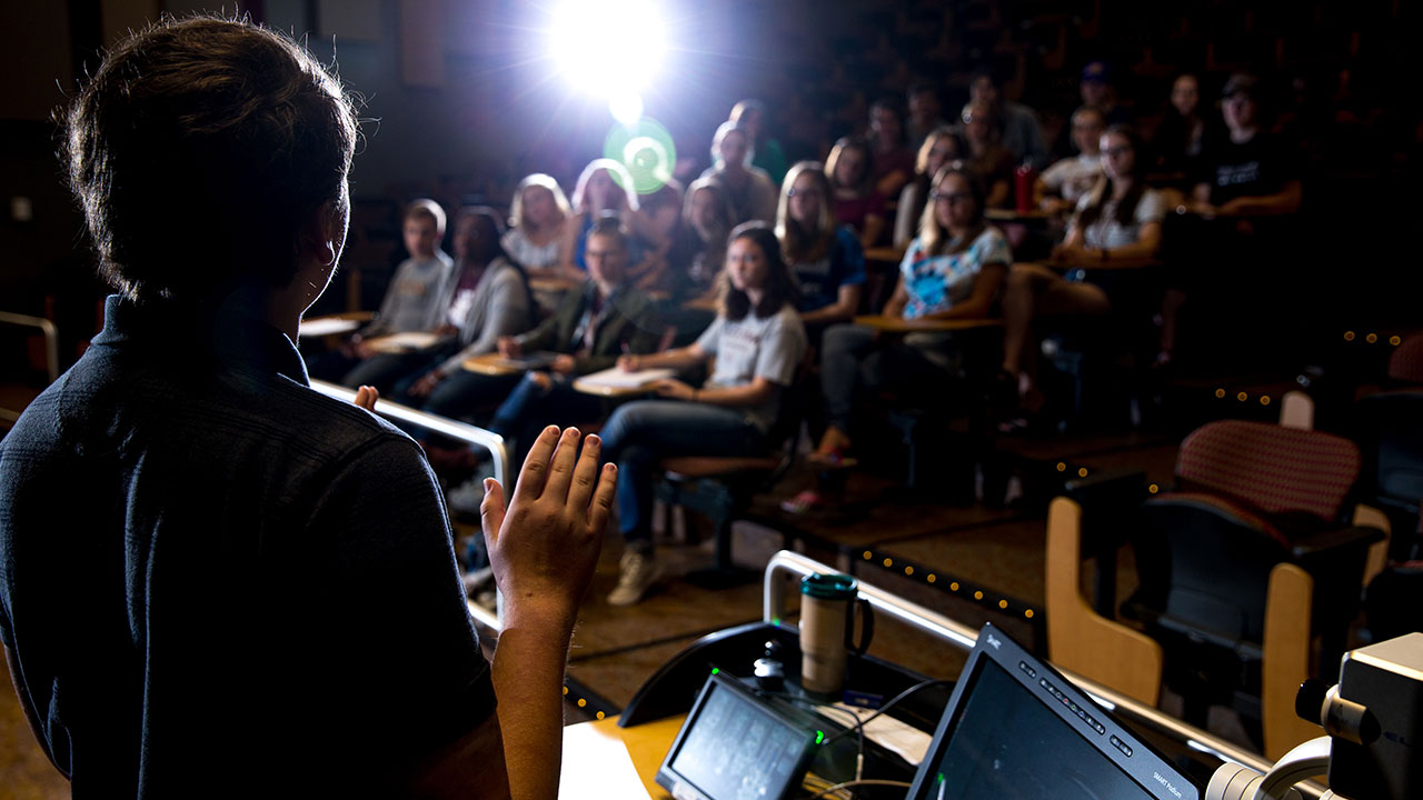 Professor lecturing to students in dark auditorium