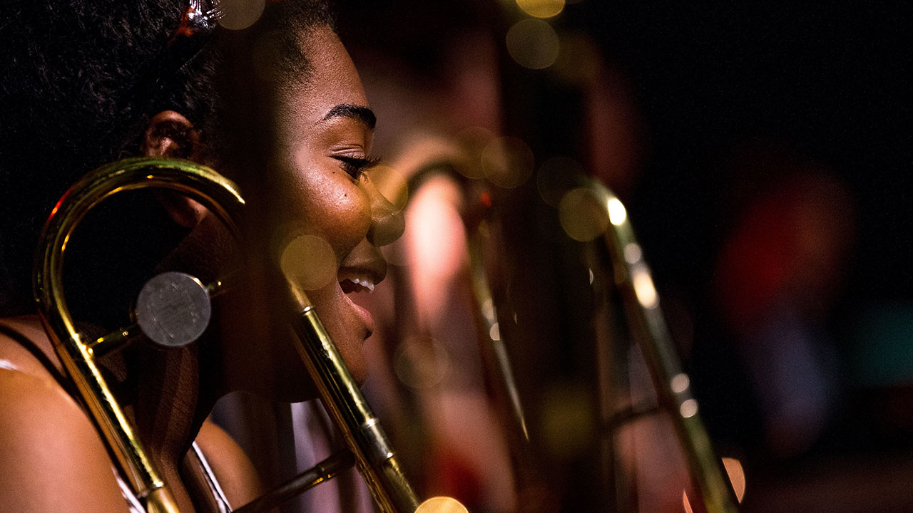 Student in brass section smiling with flare from stage lighting