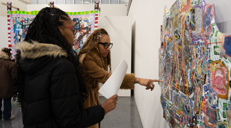 Female student and professor examine paper quilt project.
