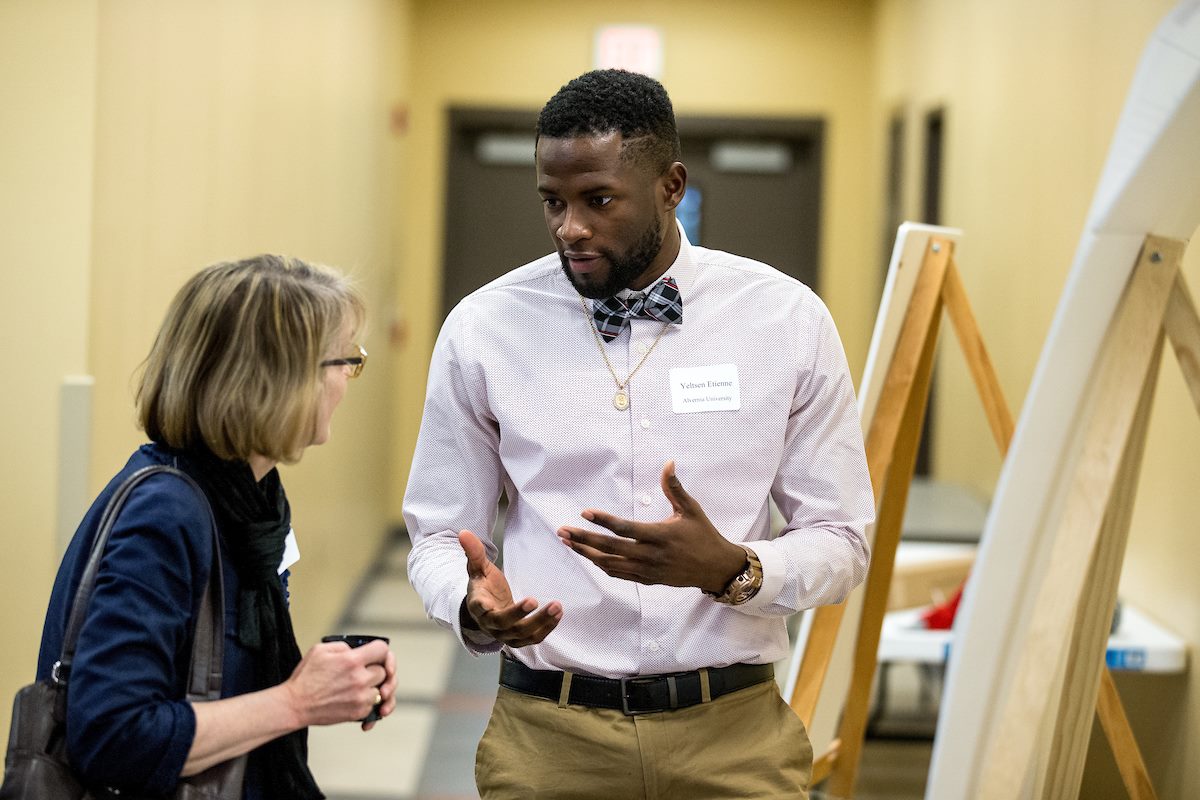 Professionally dressed Alvernia University student answers questions about his research during the poster presentation segment. 