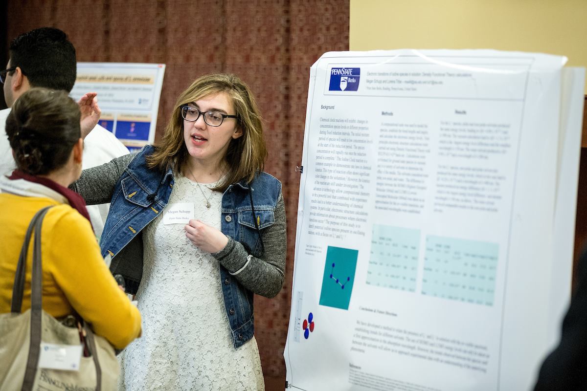 Professionally dressed Penn State Berks researcher standing in front of her poster, answering questions during the poster session. 