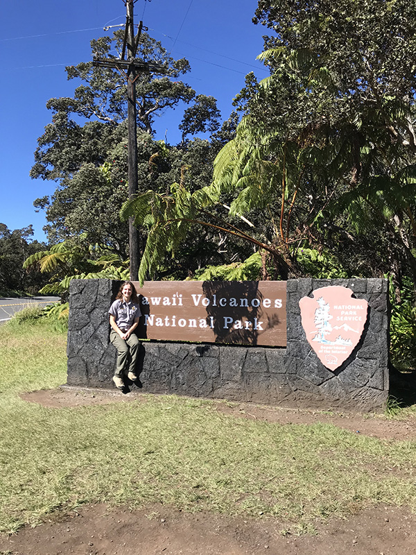 Carly Plesic sitting on the Hawaii Volcanoes National Park Sign