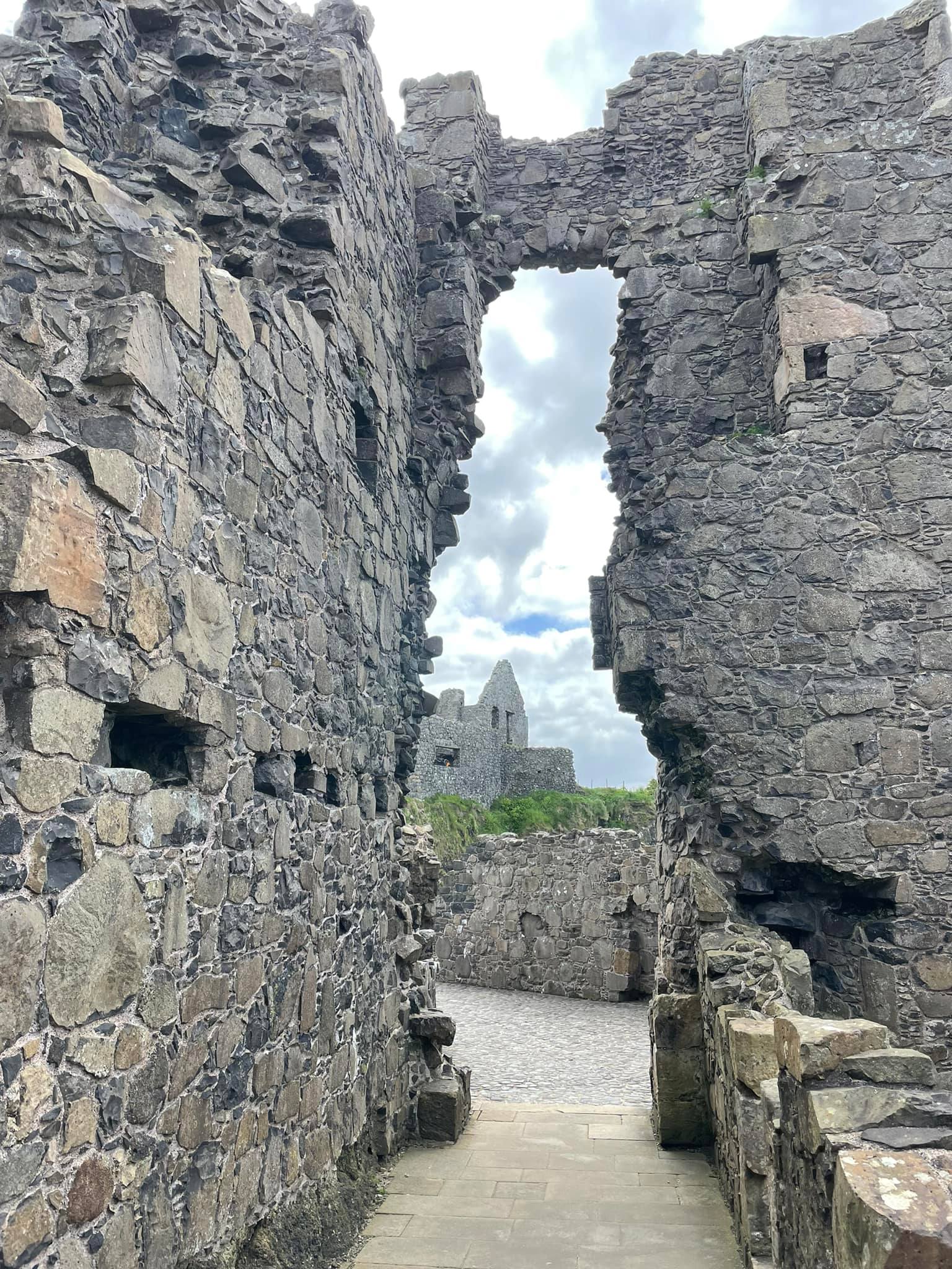 Small corridor in ancient stone castle ruins, with a stone castle tower visible in the distance