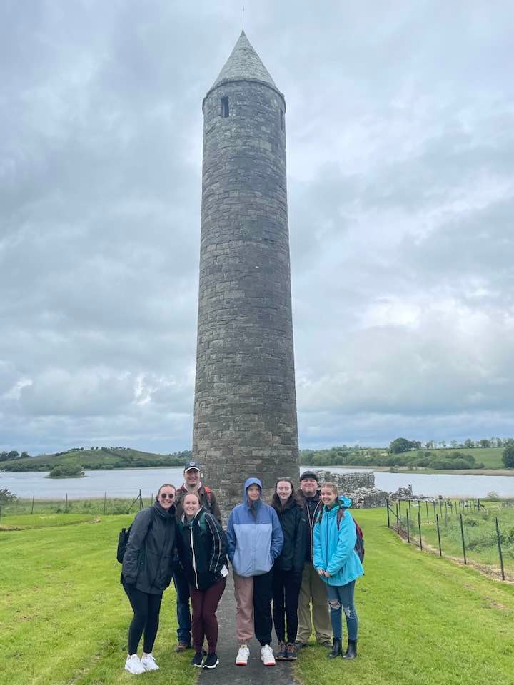 Group of students and instructors smiling together in front of a stone tower