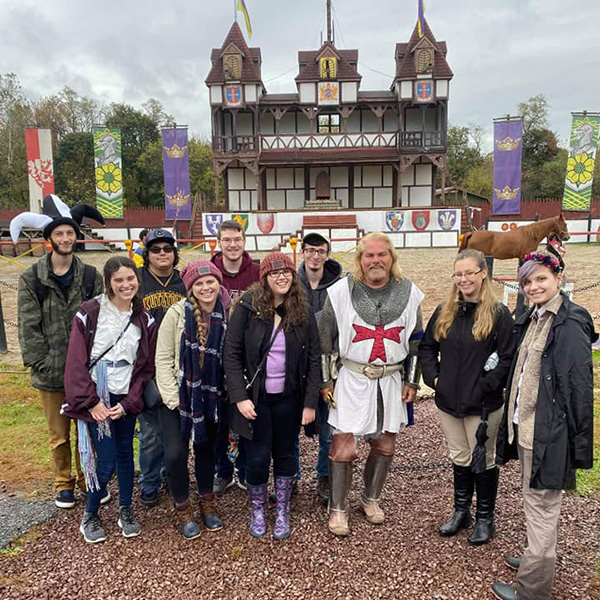 History club members smiling for a group photo with a knight in front of a castle-style building.