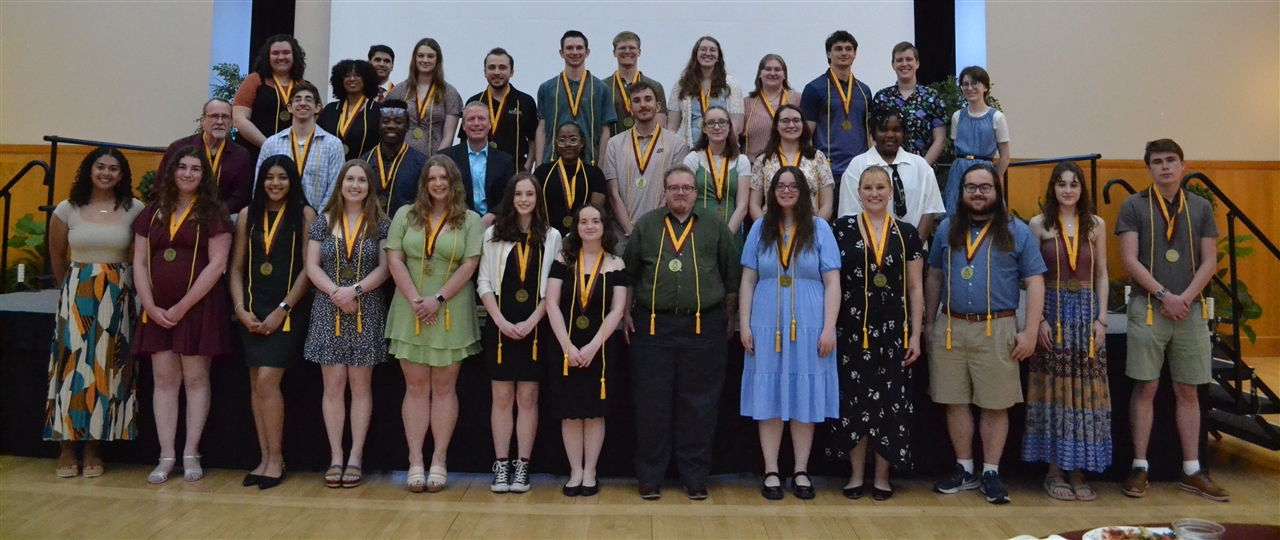 Seniors in the honors program in a group on stage in front of a slide that reads "Honors Senior Banquet Spring 2025"