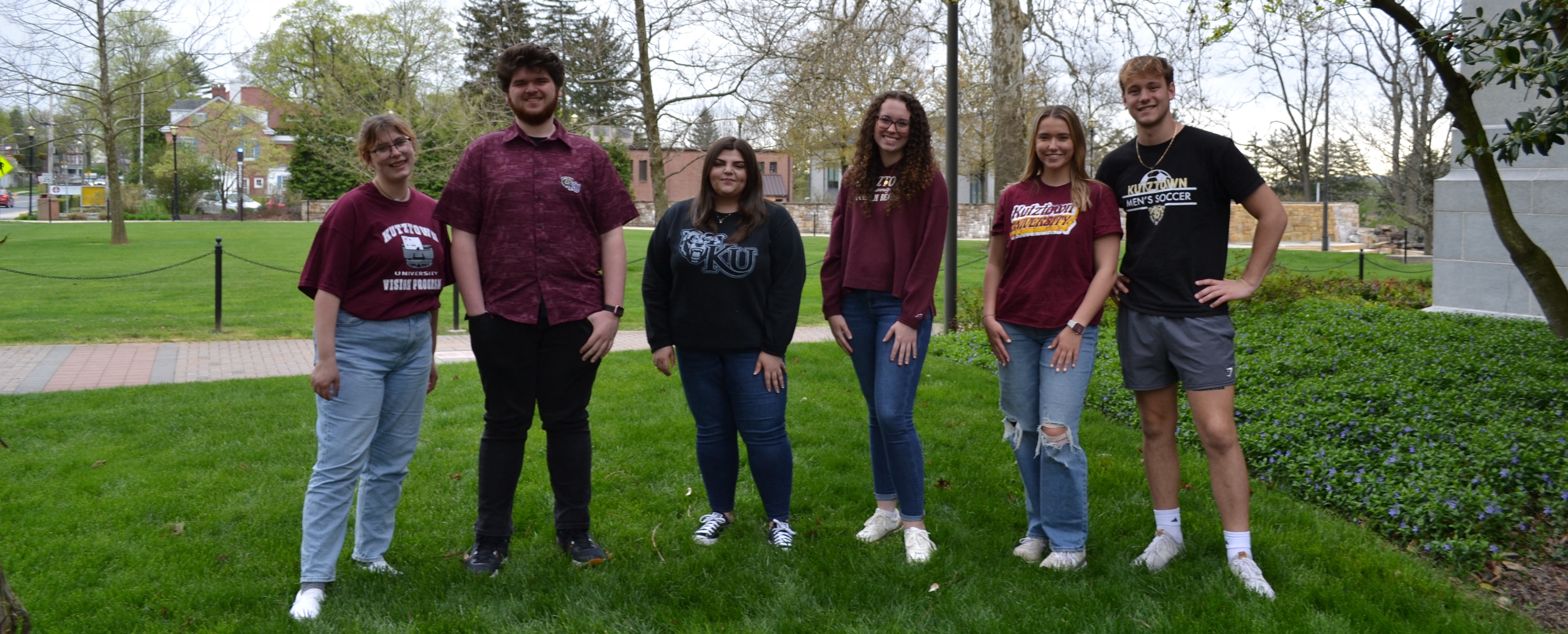 Six transfer students wearing KU gear standing and smiling in the grass behind the graduate center