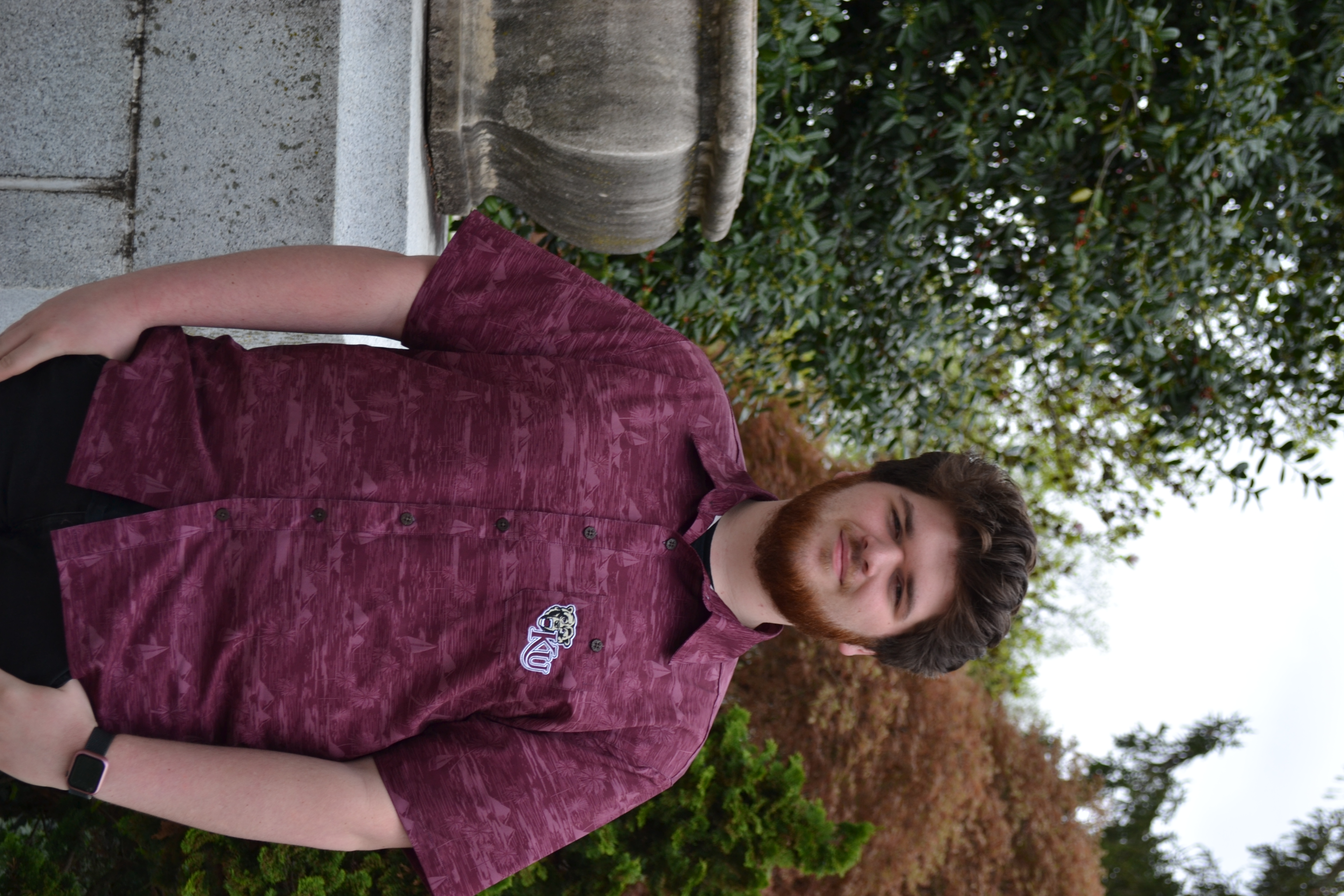 Transfer student Zach wearing a K-U button-up shirt standing outside on campus, smiling softly at the camera