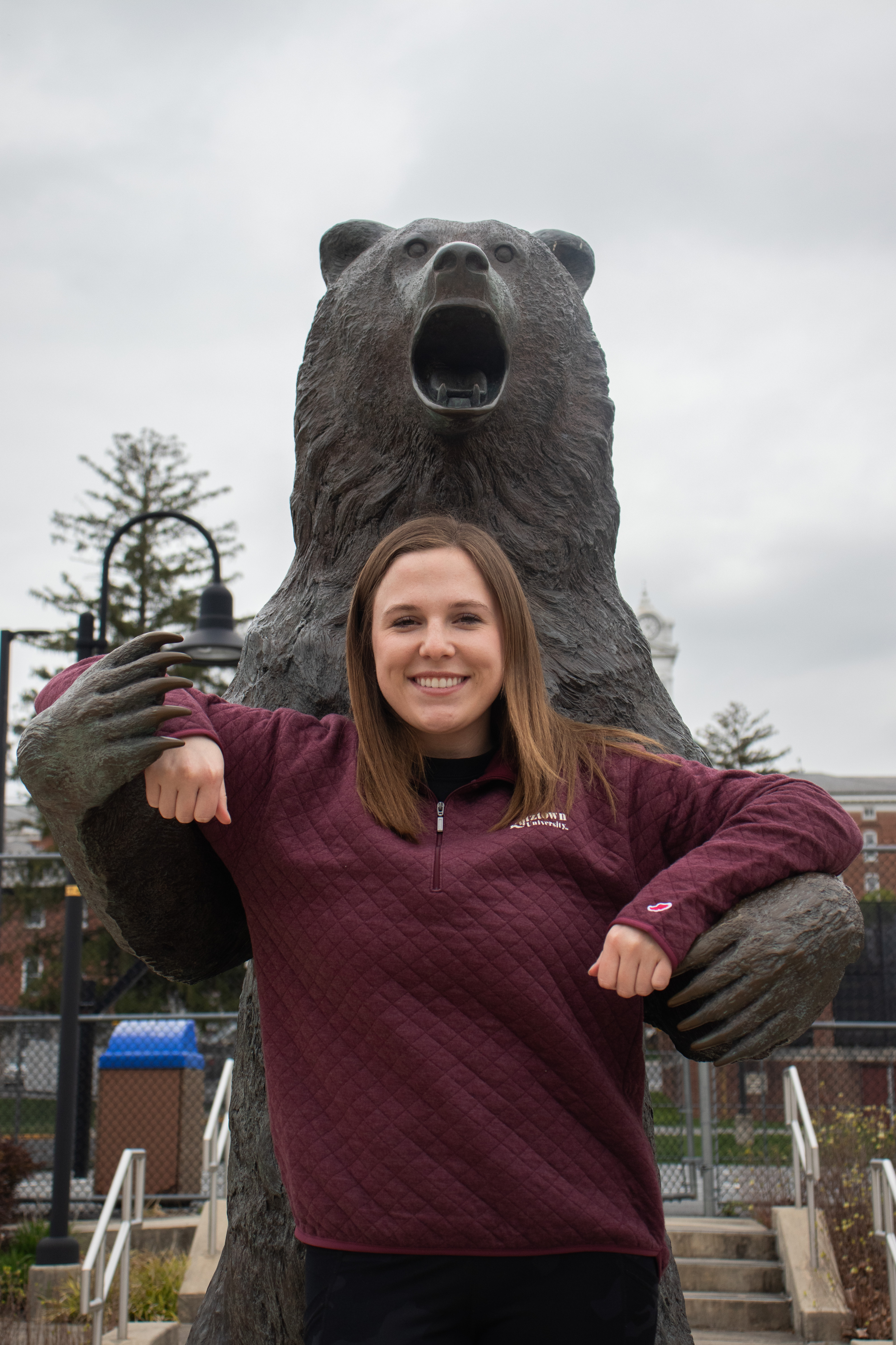 Transfer student Riley in the arms of a bronze golden bear statue wearing a maroon quarter-zip, smiling at the camera