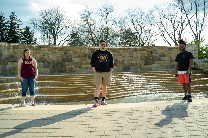 three transfer students smiling in front of the Main fountain 