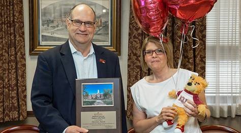 Desiree Aston holding her celebratory balloons and stuffed golden bear, while Dr. Hawkinson presents her with the Employee of the Month placard 