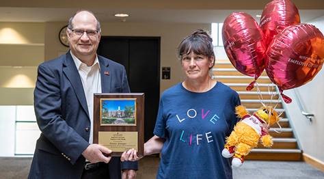  Donna Younger holding her celebratory balloons and stuffed golden bear, while Dr. Hawkinson presents her with the Employee of the Month placard 
