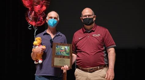  Peter Isaacson holding his celebratory balloons and stuffed golden bear, while Dr. Hawkinson presents him with the Employee of the Month placard 