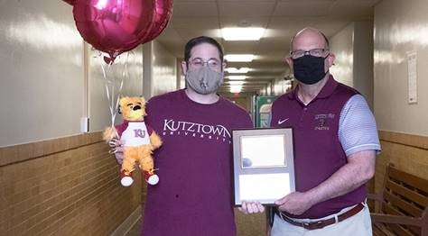 James Brenneck and Dr. Hawkinson holding the Employee of the Month placard, balloons and stuffed golden bear