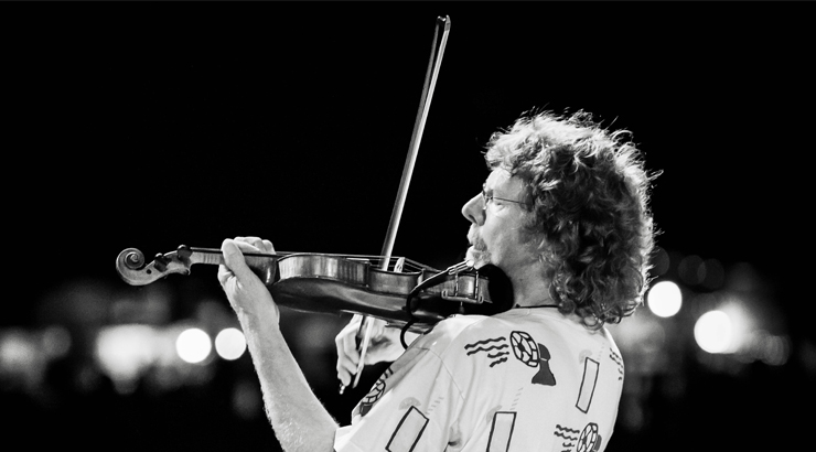 Black and white image of Sam Bush playing the violin in front of bright lights